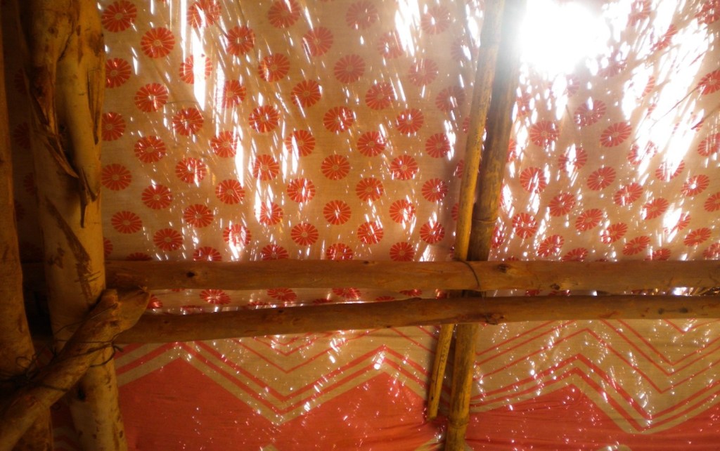 Sunshine through the patterned fabric of a tent supported by a structure of wooden poles.